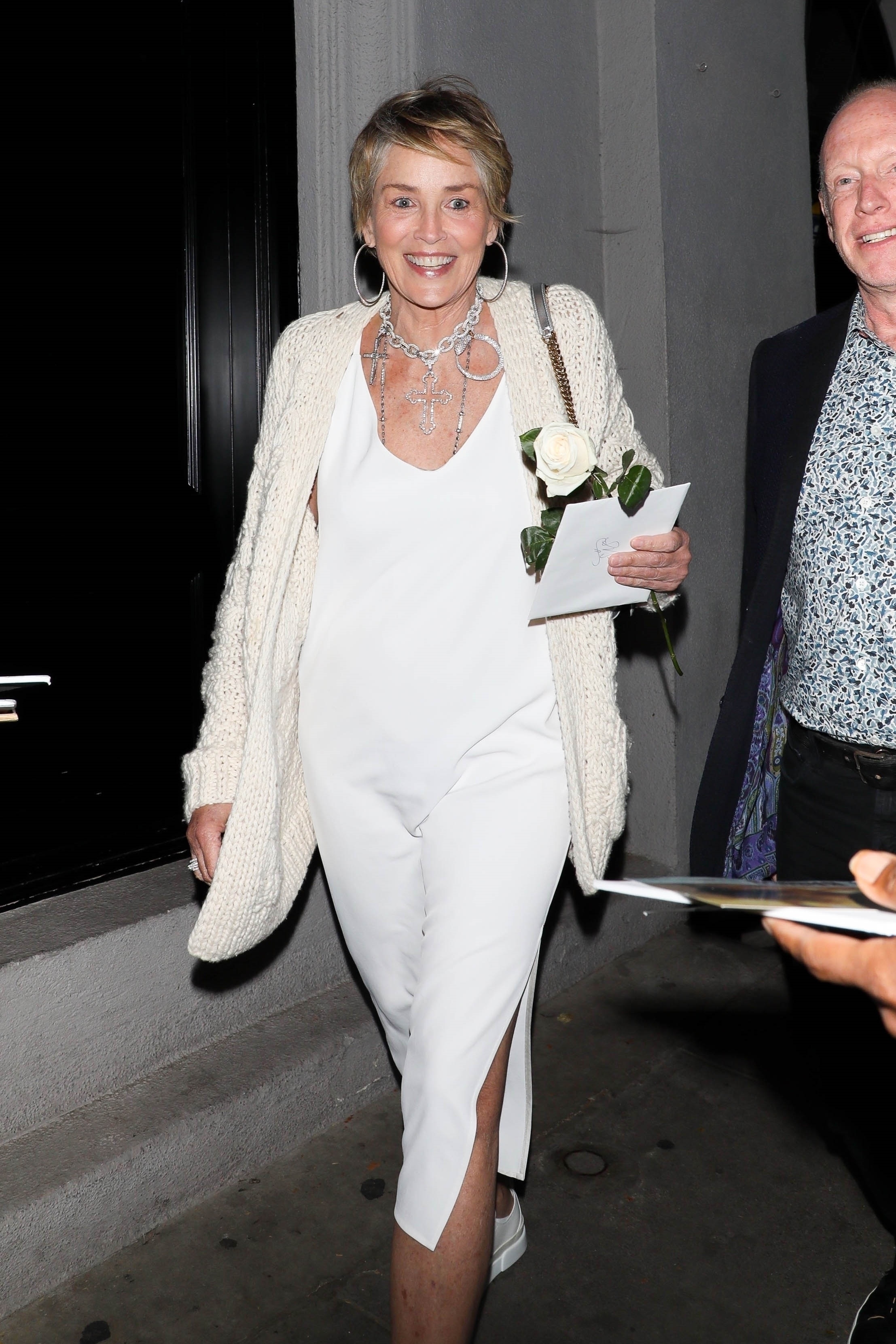 Una noche divertida. Sharon Stone fue a comer a un exclusivo restaurante de Los Ángeles y lució un look off: white de vestido, sweater y zapatillas de cuero. Además, sonrió cuando vio a los fotógrafos que la encontraron cuando abandonaba el salón con una rosa y una carta en su mano